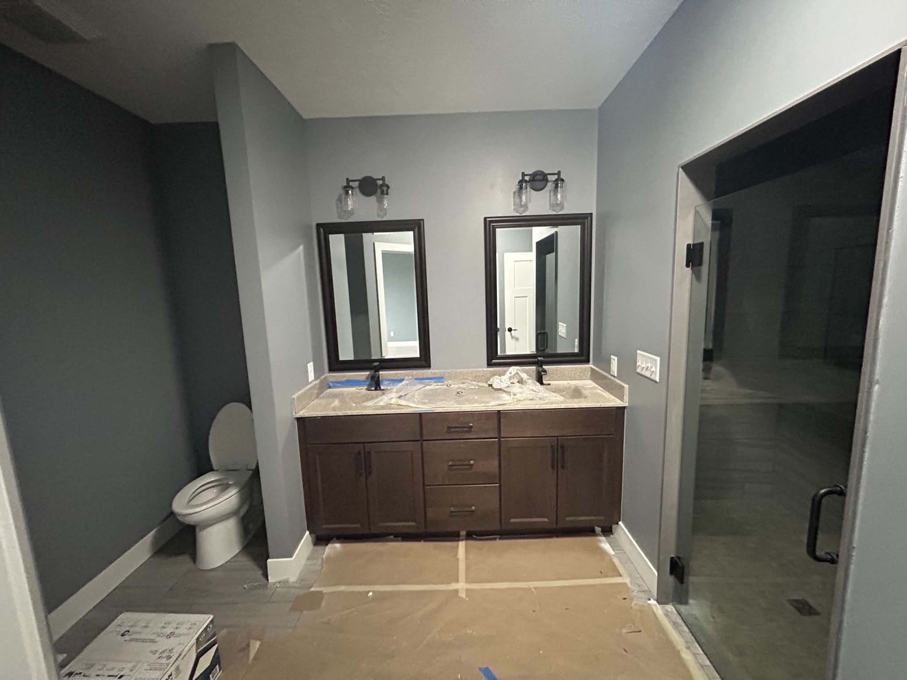 Bathroom remodel with double vanity, matte black fixtures, toilet, and glass shower