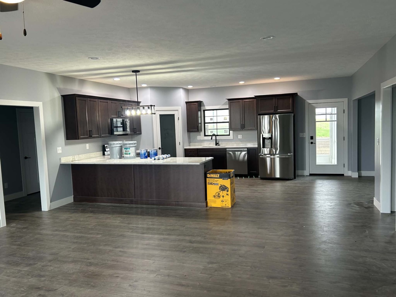 Open-plan kitchen with dark cabinets, island, stainless appliances, and plank flooring