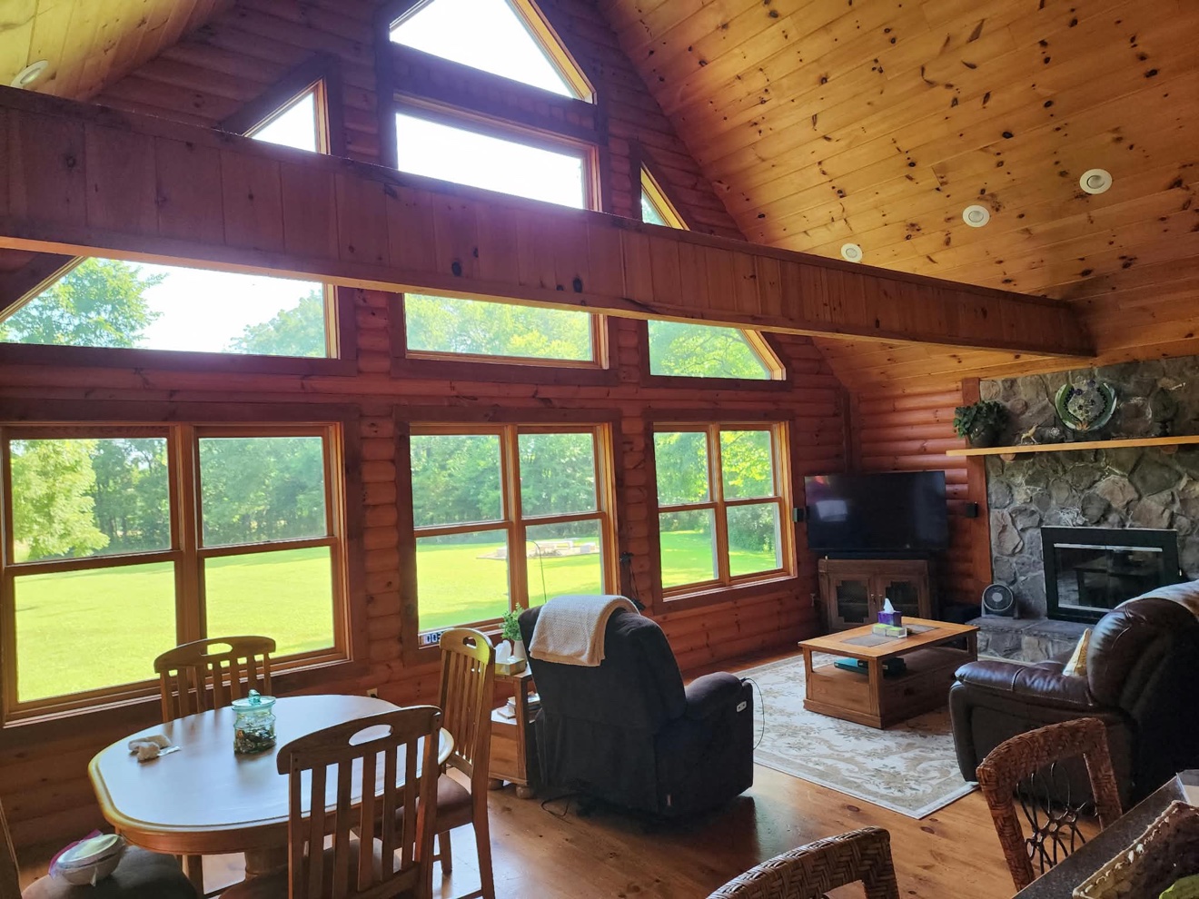 Log cabin great room with exposed beams, wood ceiling, and tall windows