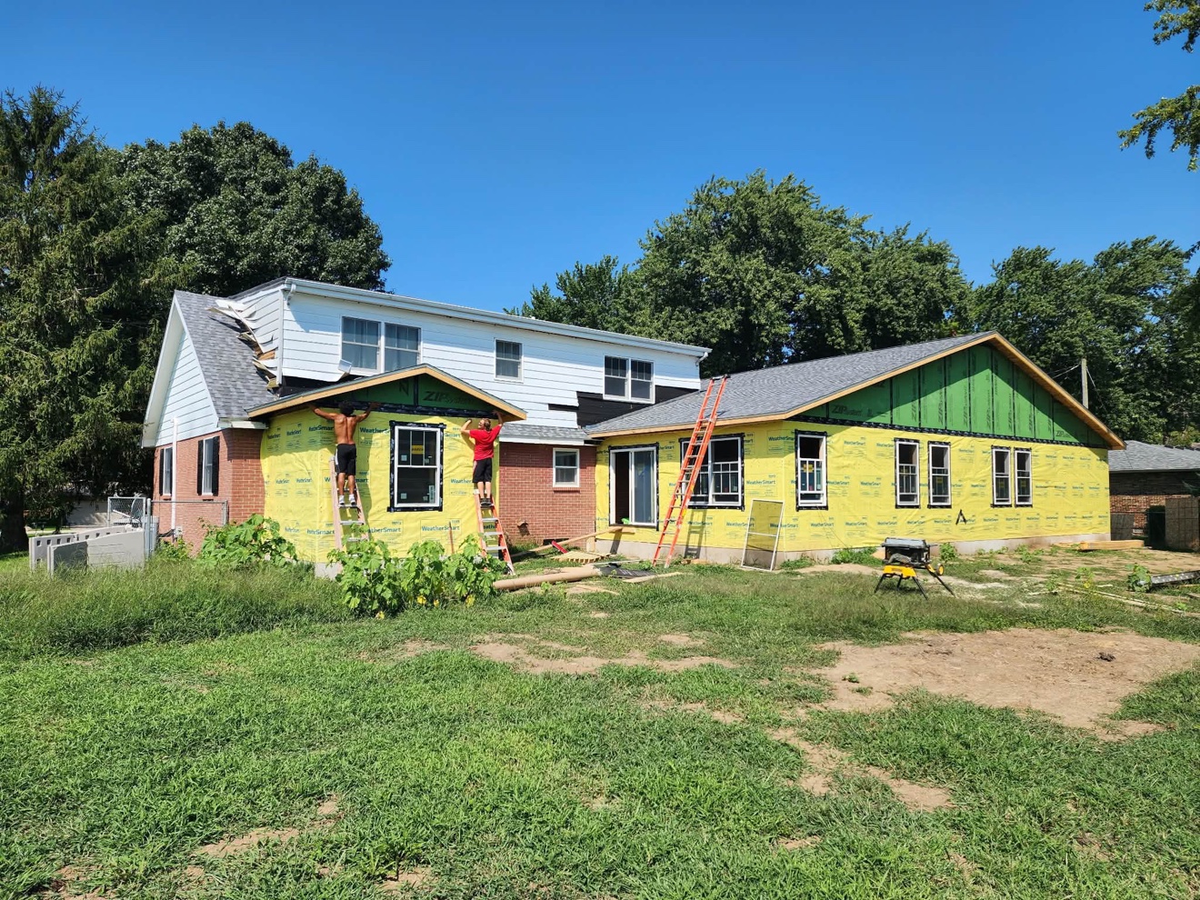 Home exterior renovation in progress with yellow house wrap and new siding sections